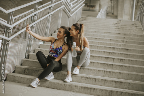 Two athlete women resting and taking selfie after jogging