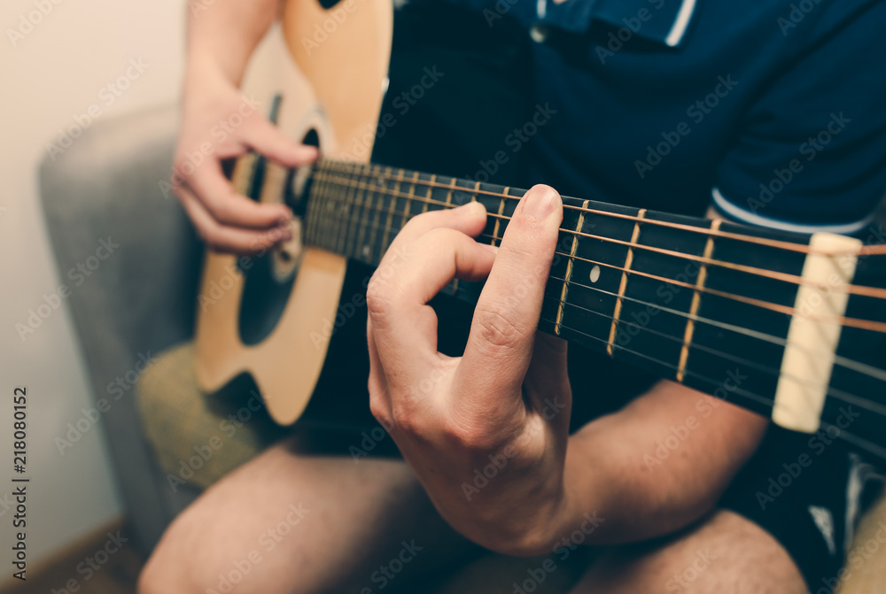 Man at home is playing the guitar. Guys hands are taking the chord on strings. Music making lifestyle concept. Free time hobby for everyone. Retro guitar photo.