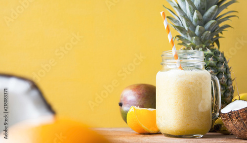 Fresh exotic smoothie with fruits and coconut milk on yellow background.