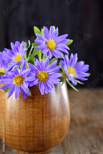 Little violet asters in a wooden vase on a table