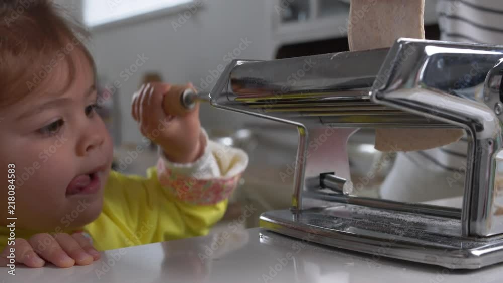 Little girl daughter with mother in home kitchen learning to use pasta maker rolling dough Little girl daughter with mother in home kitchen learning to use pasta maker rolling dough
