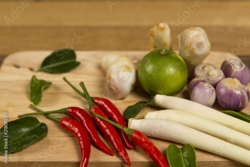 Fresh vegetables on cutting board, chili, lemon grass, lemon leaf set on wooden background. Ingredients for cooking.