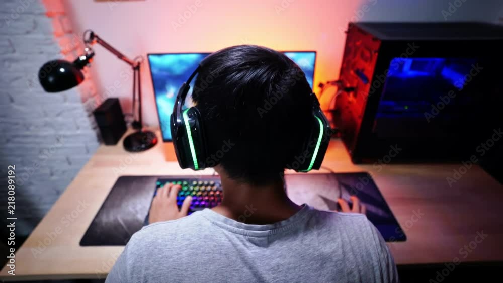 Back view of asian male gamer playing computer game by the table at home