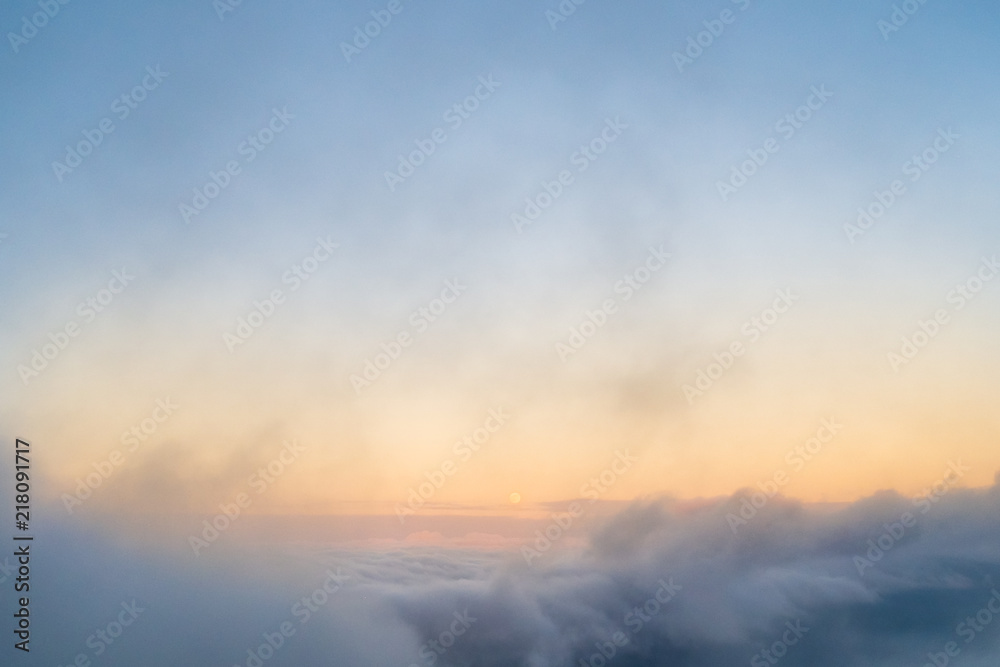 Fototapeta premium Moon rising during a sunset between some clouds with orange tone