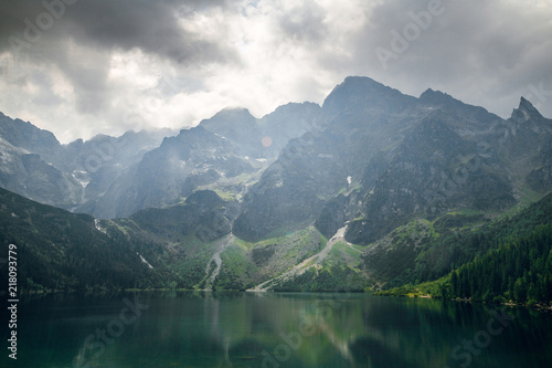 Aerial view shot of beautiful green hills and mountains in dark clouds and reflection on the lake Morskie Oko lake, High Tatras, Zakopane, Poland.