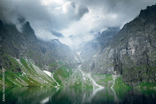 Scenic shot of beautiful green hills and mountains in white clouds and reflection on the lake Morskie Oko lake, High Tatras, Zakopane, Poland.