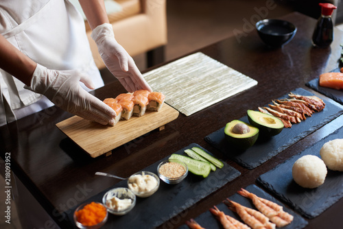 Close-up view of process of preparing rolling sushi. Chef is serving fresh delicious rolls on the wooden board.