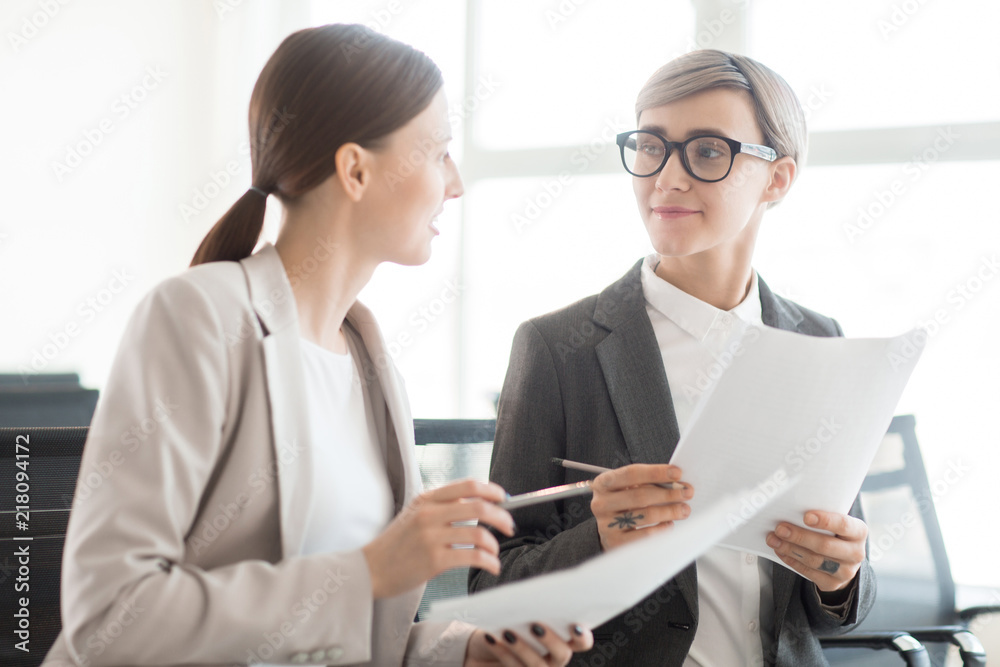 Stylish adult businesswomen sitting with documents and talking in bright daylight communicating professionally Stylish adult businesswomen sitting with documents and talking in bright daylight communicating professionally