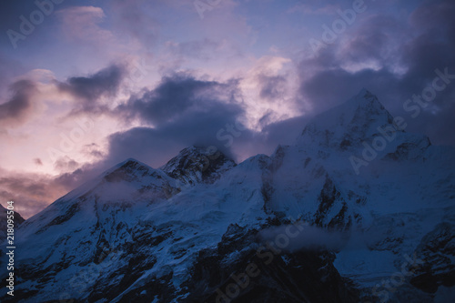 Himalayas landscape. Mountain range with trail in mist and clouds, dark sky with dim sunlight in the background. Stormy weather in mountains. Trekking in Himalaya mountains, Nepal. Nature landscape.