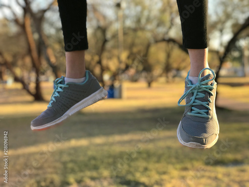 Feet with gray tennis shoes hanging in mid-air with soft-focus, green, park backgroun