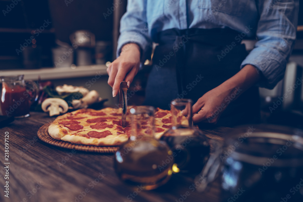 Fototapeta premium Young woman in kitchen making delicious homemade pizza on rustic kitchen table at home. Italian rural cooking still life. Chef hands preparing homemade food. Healthy foods, cooking concept.
