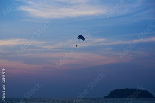 Sunset over the ocean. Silhouette of a lonely parachute on sunset background. Sky, clouds and water. Beautiful serene scene. Natural composition of nature. Landscape. Concept of outdoor activities..