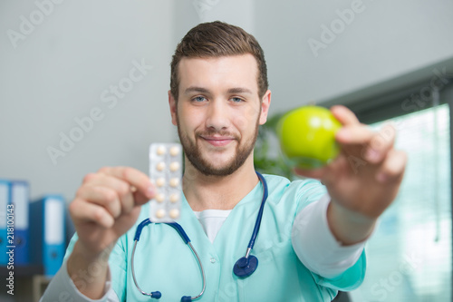 smiling male nutritionist with an apple and pills