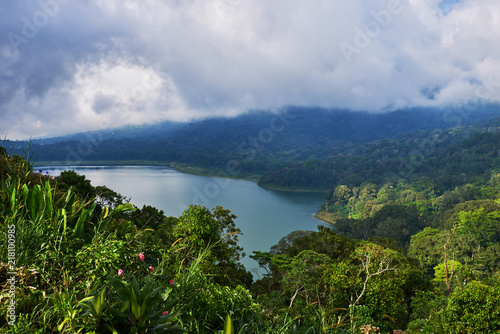 View of a lake surrounded by volcanic mountains, tropical landscape with dramatic clouds in the sky.  Lake and mountain view from a hill. Forest on the shore of a lake. Nature background.