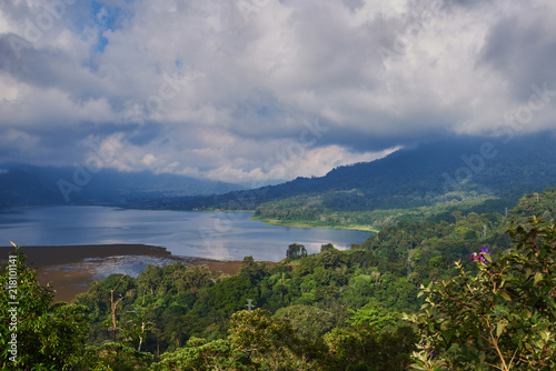 Forested mountain slope in low lying cloud with the evergreen tropical trees, shrouded in mist in a scenic landscape. Low cloud shrouds the distant mountains above the waters of the lake. © eskstock