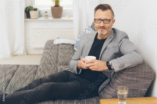 älterer mann sitzt entspannt auf dem sofa und trinkt einen kaffee