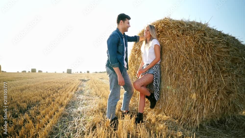 Side view of playful lovely hipster couple standing together near the hay bale on field