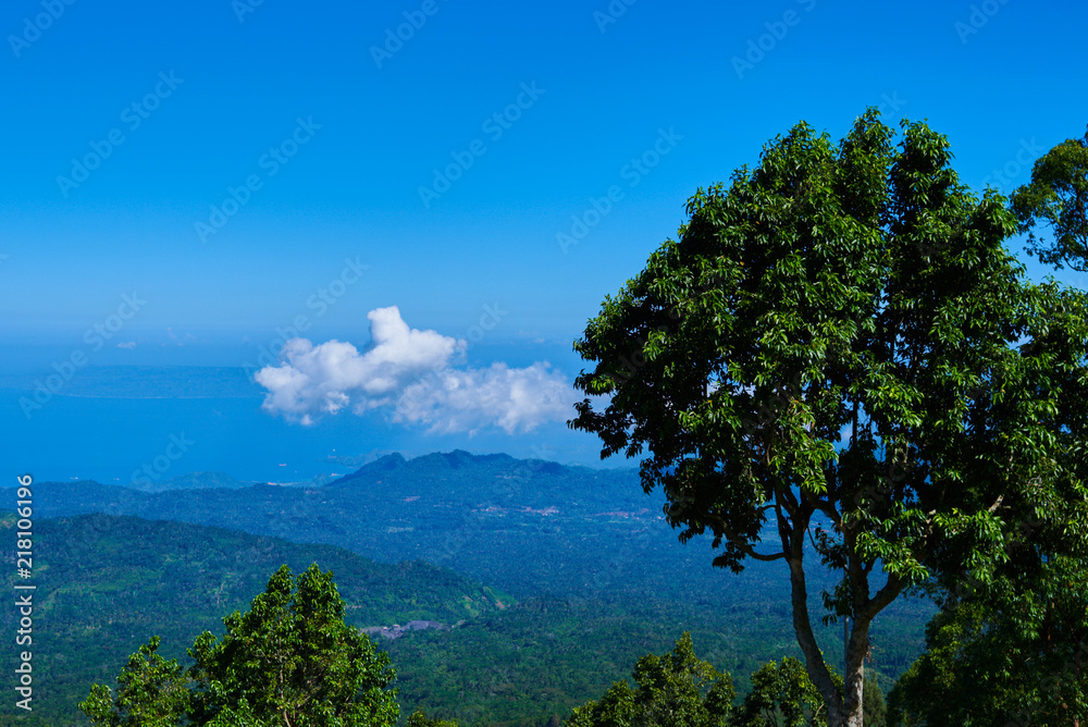 Mountainous tropical forest with blue sky and clouds in valley, high elevation landscape, panoramic view. Tourist lookout towards mountain ranges and hills covered by evergreen rainforests.