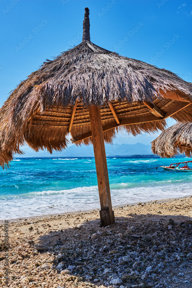 Closeup thatched beach umbrellas against the backdrop of a turquoise ocean on a clear sunny day. Empty  sandy beach with straw parasol at the coast on the paradise tropical island. Travel concept.