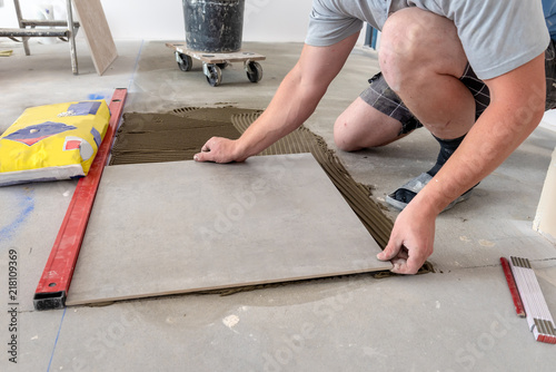 The hands of the tiler are laying the ceramic tile on the floor.