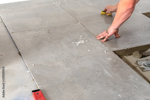 The hands of the tiler are laying the ceramic tile on the floor.