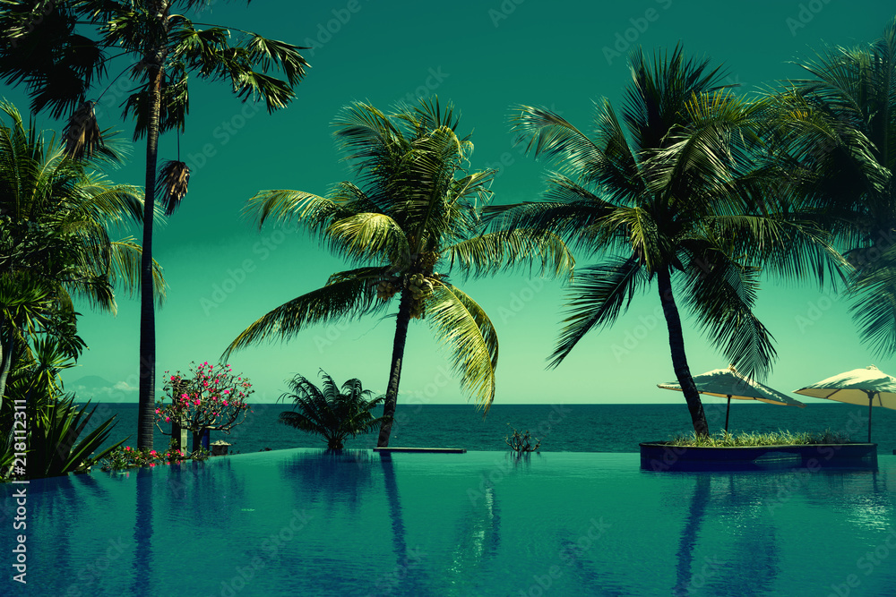 Reflection of coconut trees in turquoise color swimming pool. Beautiful wiev at a beach resort in tropics. Palm tree and luxury hotel swimming pool at vacation times. Summer, vacation, travel concept