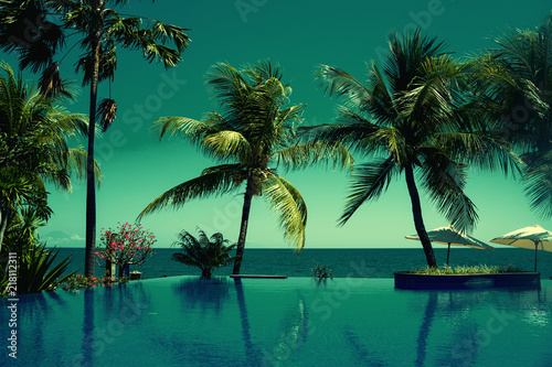 Reflection of coconut trees in turquoise color swimming pool. Beautiful wiev at a beach resort in tropics. Palm tree and luxury hotel swimming pool at vacation times. Summer, vacation, travel concept