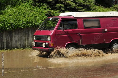 rotes Auto fährt durch eine überflutete Straße mit braunem Wasser vom Hochwasser © Mitch Shark