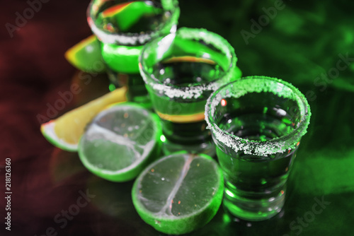 Tequila and limes on a bar in green light and smoke photo