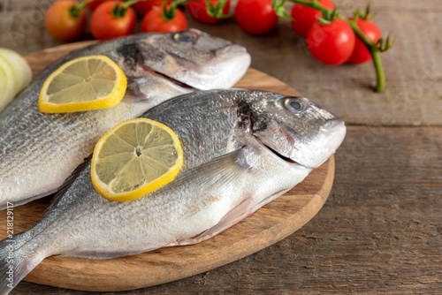 Fresh dorada fish with vegetables on wooden background.