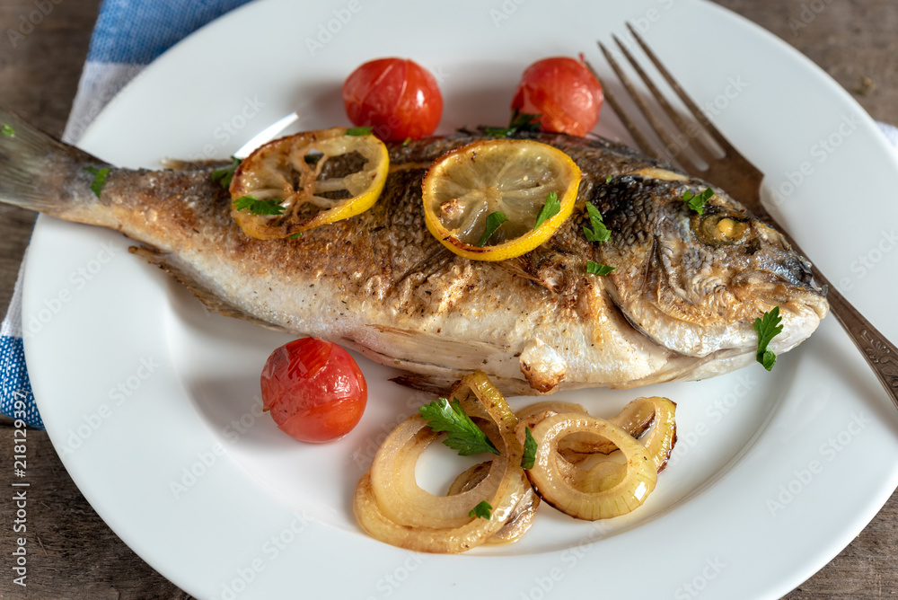 Dorada on plate with onions, lemon and cherry tomatoes Dorada on plate with onions, lemon and cherry tomatoes