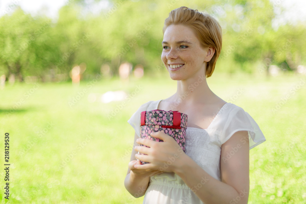 This is for you. Attractive young woman holding a gift box in her hands standing against summer green park This is for you. Attractive young woman holding a gift box in her hands standing against summer green park
