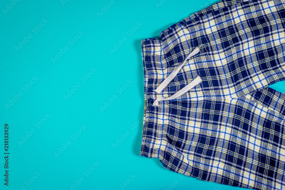 Top view of checkered sweatpants on turquoise pastel background. Children's folded sweatpants with visible two legs. Top view of checkered sweatpants on turquoise pastel background. Children's folded sweatpants with visible two legs.