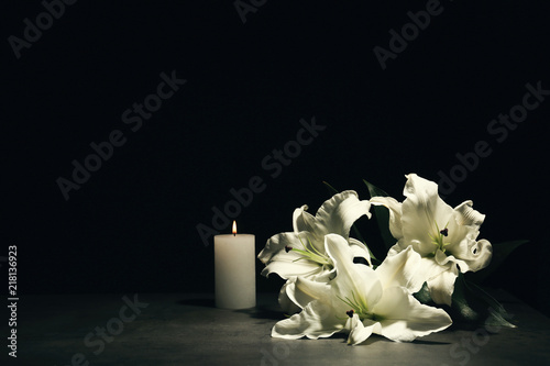 Beautiful lilies and burning candle on dark background with space for text. Funeral flowers