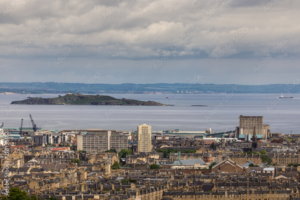 Edinburgh, Scotland, UK - June 13, 2012: Looking from Calton Hill over densely built Leith suburb towards the Nord Sea inlet under a heavy cloudscape. Island and other side of water are mostly green.