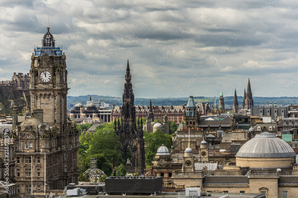 Obraz premium Edinburgh, Scotland, UK - June 13, 2012: Looking from Calton Hill upon the Balmoral Clock Tower along Princess street. Black Scott Monument. Green hills on horizon. Heavy Cloudscape.