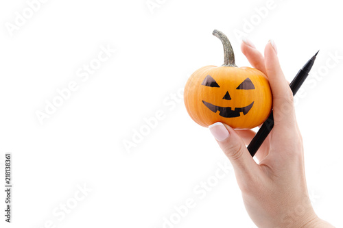 Woman's hand holding small painted halloween pumpkin and black marker pen isolated on white background. Holiday decoration concept. photo