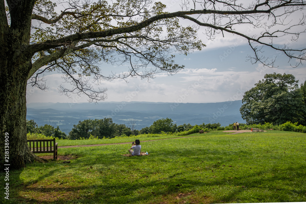 A woman sits on a blanket beneath a tree relaxing in the summer sun as she enjoys the view of the Appalachian Mountains from Shenandoah National Park and Skyline Drive A woman sits on a blanket beneath a tree relaxing in the summer sun as she enjoys the view of the Appalachian Mountains from Shenandoah National Park and Skyline Drive