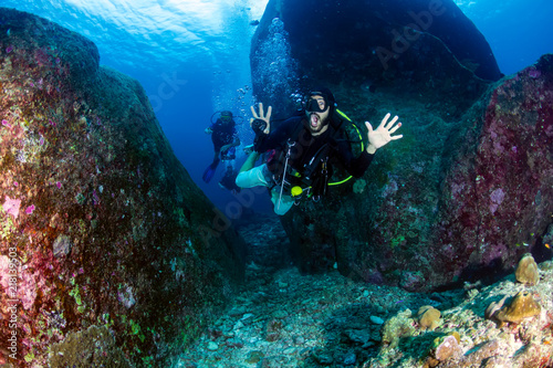 A SCUBA diver exiting an underwater tunnel on a deep, dark tropical coral reef
