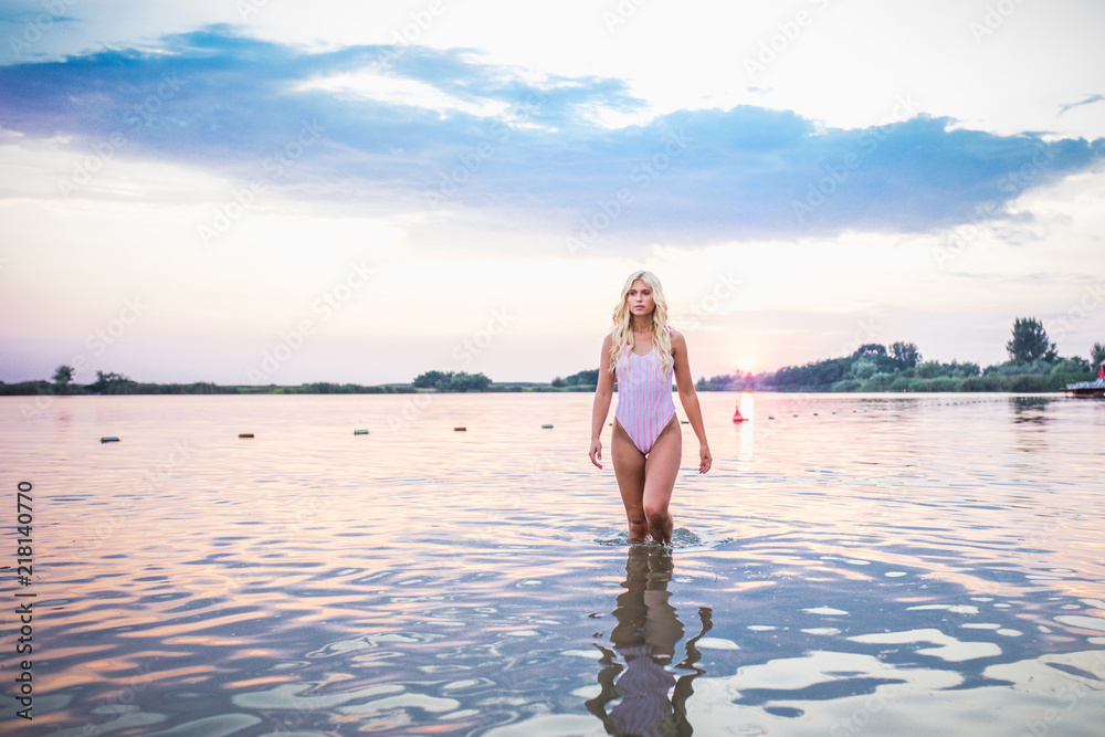Fototapeta premium Attractive girl posing in water at sunset