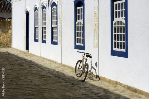 Bicycle parked next to the white wall with blue windows