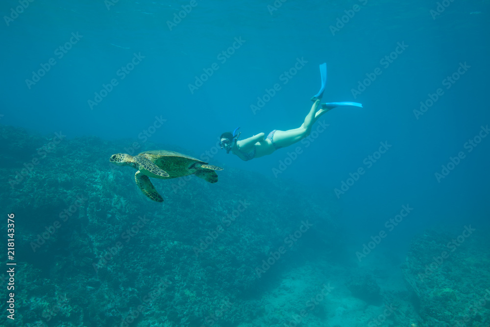 Woman in bikini swims underwater with wild green sea turtle