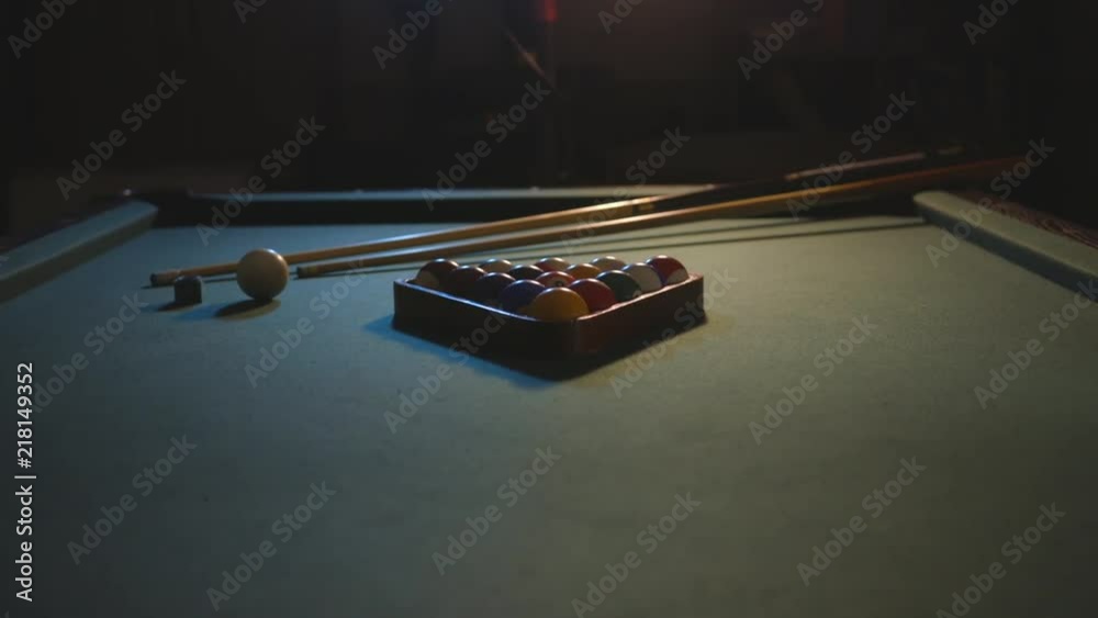 A slide in shot of a pool table in a dark basement. The setting is meant to feel cool or edgy.