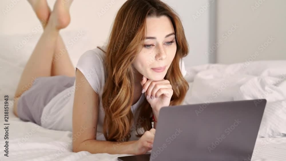 Young happy brunette lady lying on bed at home and making videocall with laptop computer
Young happy brunette lady lying on bed at home and making videocall with laptop computer