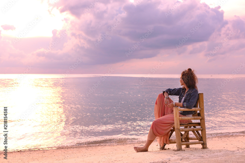 beautiful young woman sitting in chair on the beach at sunset