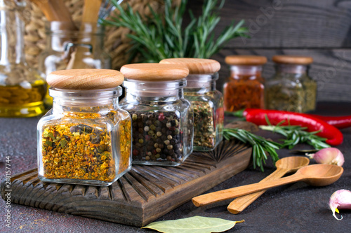 Products for cooking in kitchen, kitchen utensils, herbs, colorful dry spices in glass jars on dark background