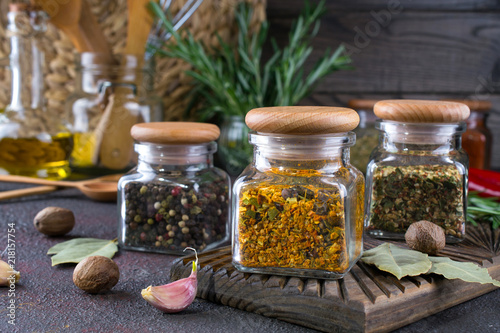 Products for cooking in kitchen, kitchen utensils, herbs, colorful dry spices in glass jars on dark background