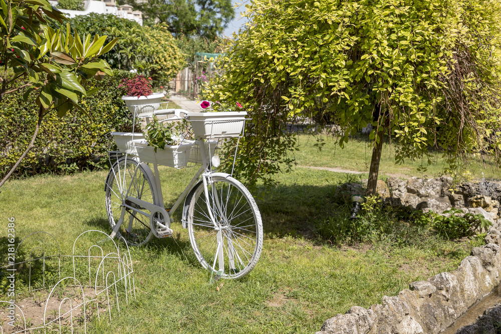 Vintage white bicycle with baskets of flowers in the garden. Beautiful decoration on a natural background