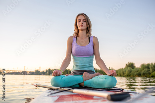 Young beautiful woman meditating in a sea at SUP paddleboarding. Healthy lifestyle.