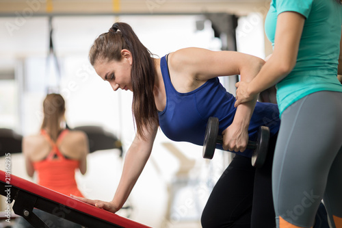 Fitness trainer helping young girl doing exercises on bench in gym